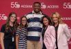 Five people smile and pose together in front of a red step-and-repeat backdrop featuring the ACCESS 55th anniversary logo. The group includes four women and one man, with the man standing in the center wearing a navy-and-white striped shirt.